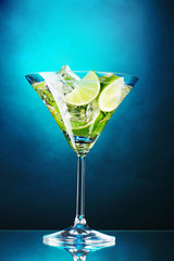 glass of cocktail with lime and mint on blue background