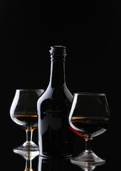 Glasses of brandy and bottle on black background
