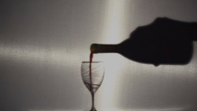 Silhouette of a glass and wine poured by a hand