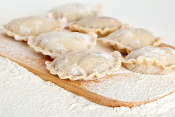Fototapeta na wymiar Dumplings (vareniki) in flour on wooden board