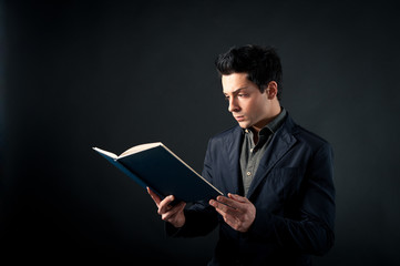 Young man reading a book against dark background.