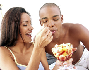 Pareja hispana compartiendo y comiendo ensalada de frutas.