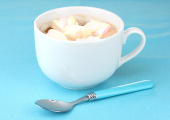 Cup of cappucino with marshmallows and spoon on blue background