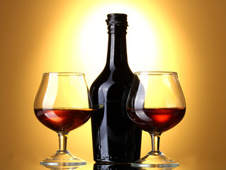 Glasses of brandy and bottle on yellow background