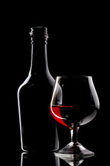 Glass of brandy and bottle on black background