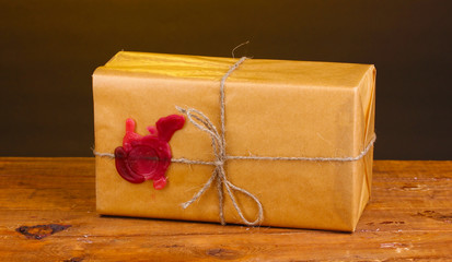 Parcel with sealing wax on wooden table on brown background