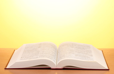 Open book on wooden table on yellow background