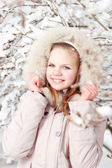 Beautiful young girl in a hood on a background a snow-bound tree