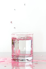 Glass of fresh ice water with splash in a pink light