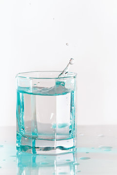 Glass of fresh ice water with splash in a turquoise light