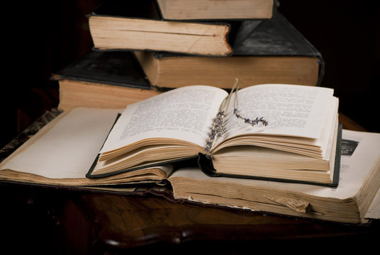 Pile old books and branches of lavender on dark background