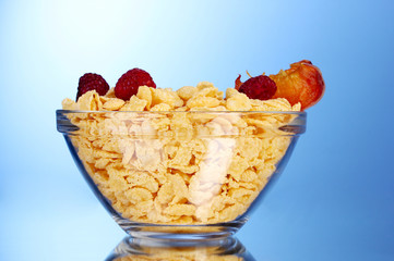 tasty cornflakes and fruit in glass bowl on blue background