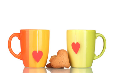 Two cups with tea bag and heart-shaped cookies isolated on white