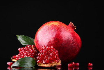 ripe pomegranate fruit with leaves on black background