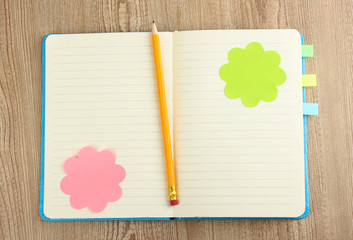 Open note book with stickies and pencil on wooden background