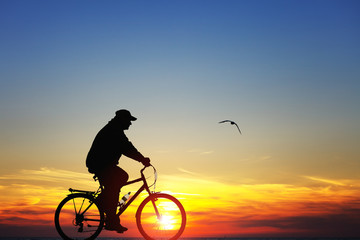 Naklejka na ściany i meble Sylwetka człowieka na rowerze o zachodzie słońca