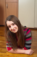 Cute smiling teenage girl lying on the wooden floor of her room