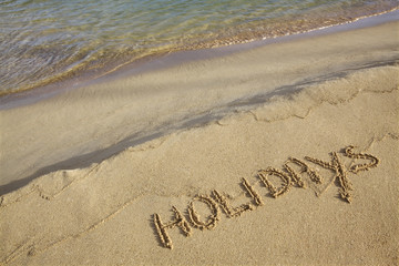 Holidays written in the sand with wave