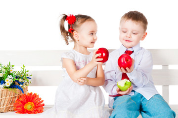 Boy and girl sitting on a bench with red apples
