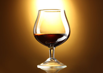Glass of cognac on yellow background