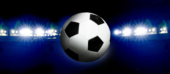 Fototapeta premium Soccer ball and illuminated stadium at night