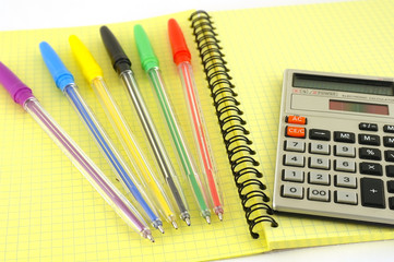 Old calculator and color pens on the yellow writing-book