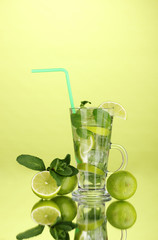Glass of cocktail with lime and mint on green background