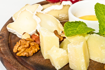 Various types of cheese with honey, nuts and grapes on plate, is