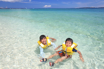 澄んだ海と海水浴を楽しむ笑顔の姉弟