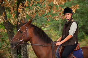Young woman riding a horse through woodland