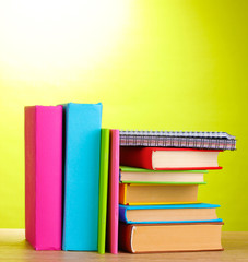 Books with stationery on wooden table on green background