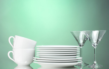 Clean plates, cups and glasses on green background