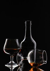 Glasses of brandy and bottle on black background