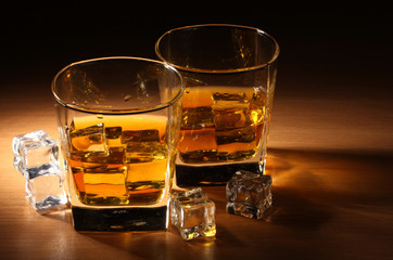 two glasses of scotch whiskey and ice on wooden table