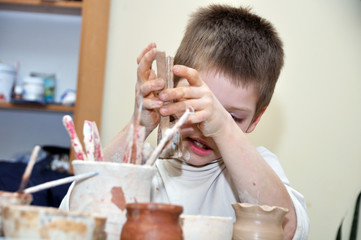 child  boy shaping clay in pottery studio