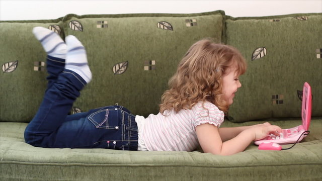 little girl lying on bed with laptop