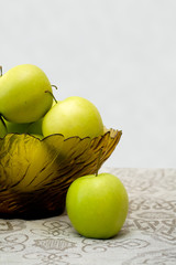 green apples in a glass vase on the table cloth
