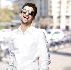 portrait of young man with sunglasses laughing at city