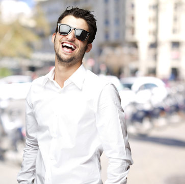 portrait of young man with sunglasses laughing at city