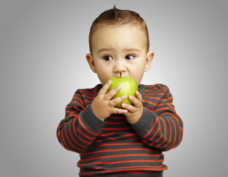 portrait of a handsome kid bitting a green apple over grey backg
