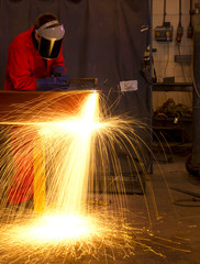 Welder bends to cut metal beam with orange sparks.