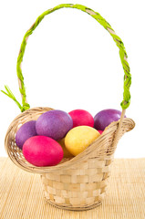 Colored easter eggs in basket on bamboo mat