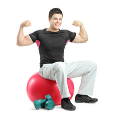 A young bodybuilder gesturing and seated on a pilates ball