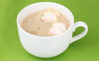Cup of cappucino with marshmallows on green background