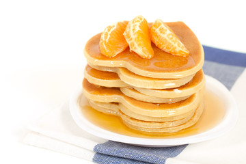 A stack of pancakes with maple syrup and tangerine.