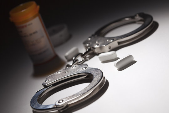 Handcuffs, Medicine Bottle and Pills Under Spot Light