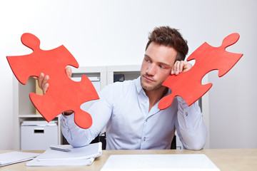 Nachdenklicher Mann im Büro mit Puzzleteil