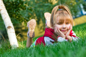 The small beautiful girl sits on a green lawn and laughs