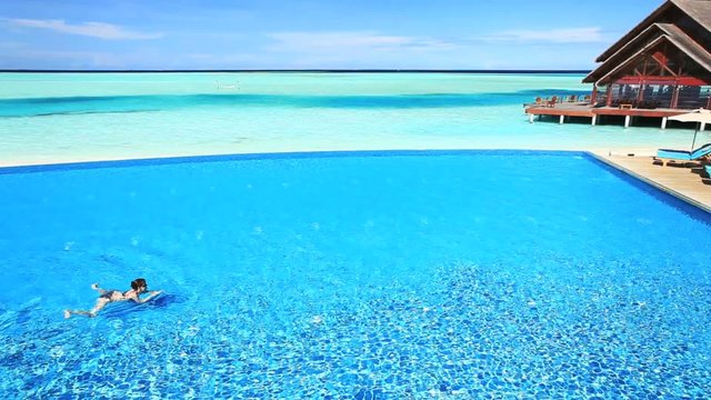Young woman swimming across infinity pool in tropics