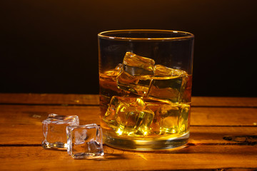 glass of whiskey and ice on wooden table on brown background